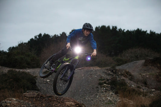 Mountainbiker mit Helm und heller Fahrradlampe springt auf Waldweg bei Dämmerung
