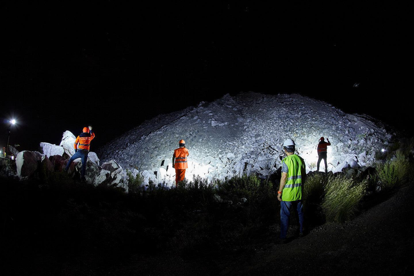 Nachtschicht Baustellenarbeiter mit Schutzhelmen und Warnwesten beleuchten Steinbruch mit Taschenlampen