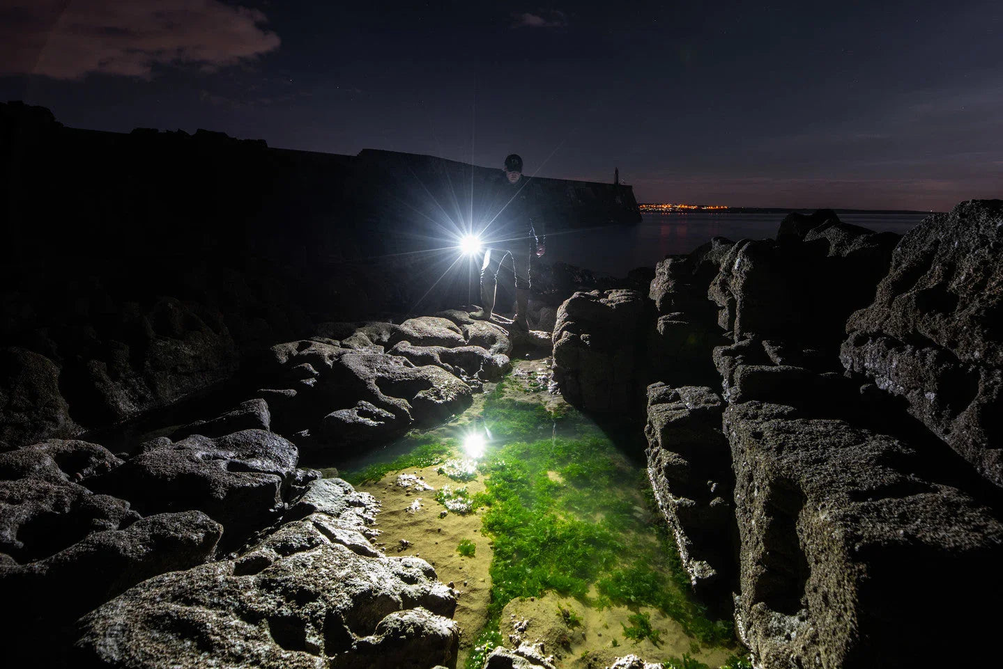 Kind in Tarnkleidung wärmt Hände am Lagerfeuer bei Nacht mit Fenix Stirnlampe in freier Natur