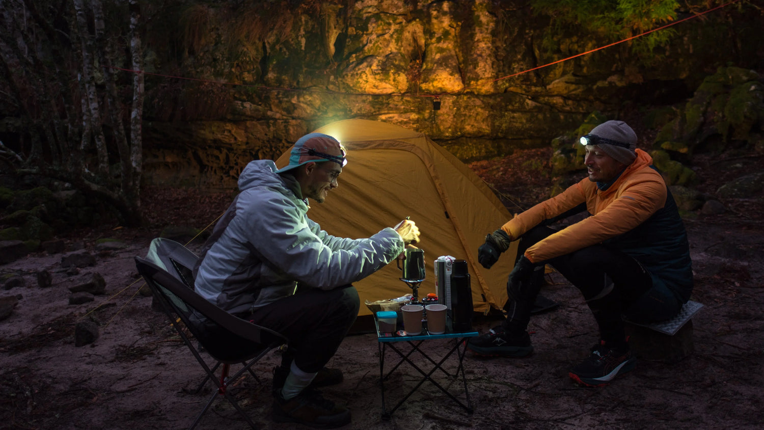 Kind in Tarnkleidung wärmt Hände am Lagerfeuer bei Nacht mit Fenix Stirnlampe in freier Natur