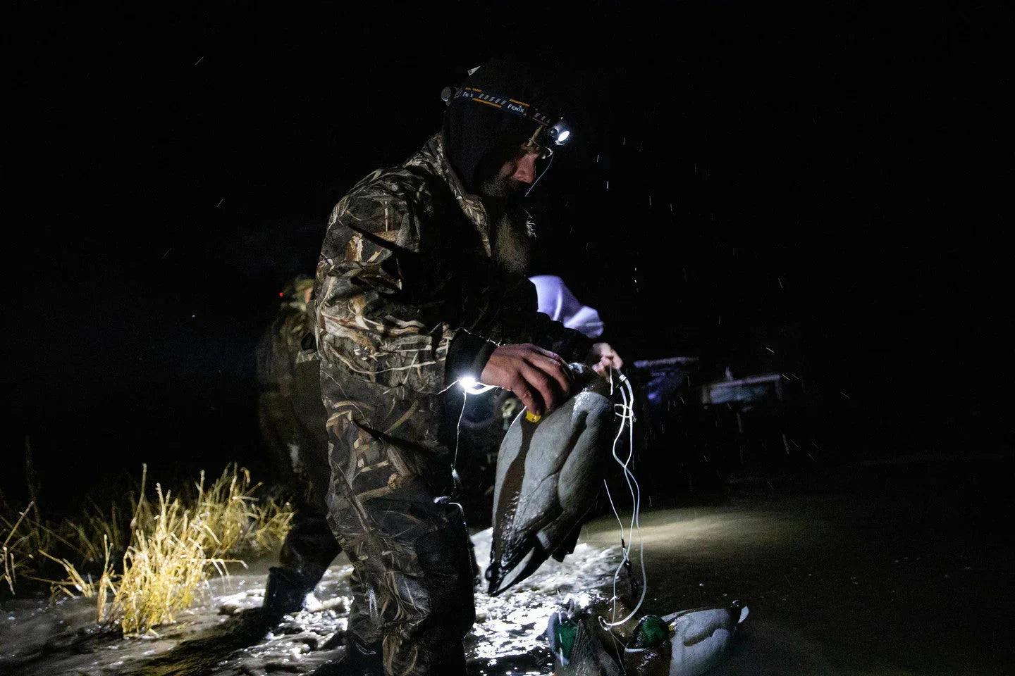 Mann mit Fenix Stirnlampe hält Waffe in dunkler Nacht mit blauem Himmel und Ausrüstung