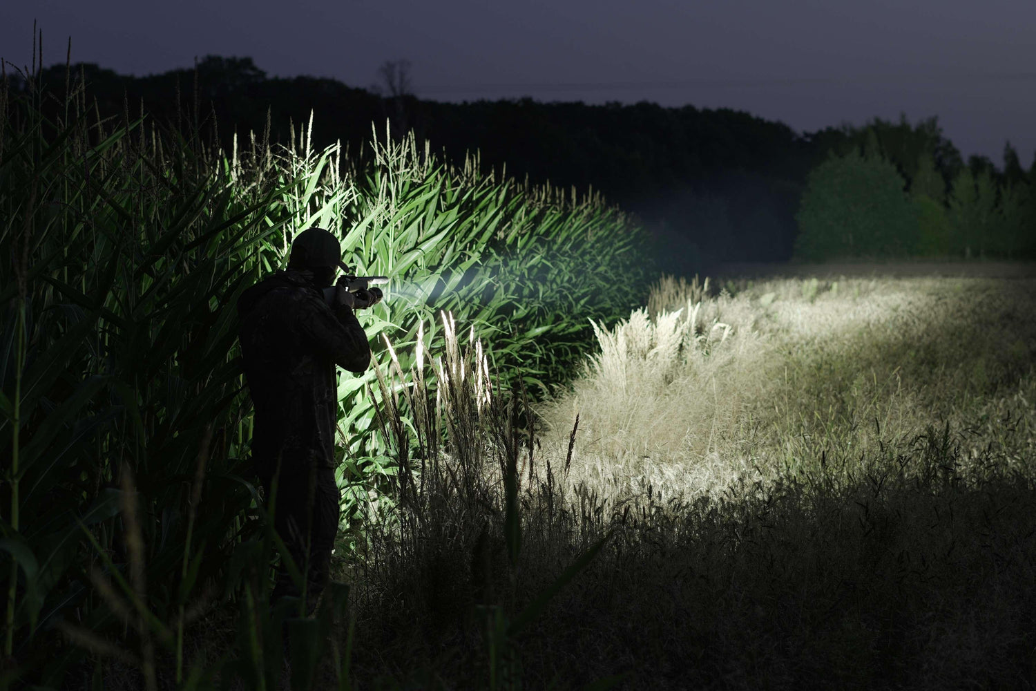 Mann mit Fenix Stirnlampe hält Waffe in dunkler Nacht mit blauem Himmel und Ausrüstung