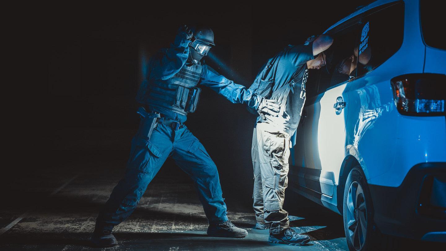 Polizist durchsucht Verdächtigen an weißem Auto nachts mit Schutzkleidung und Helm