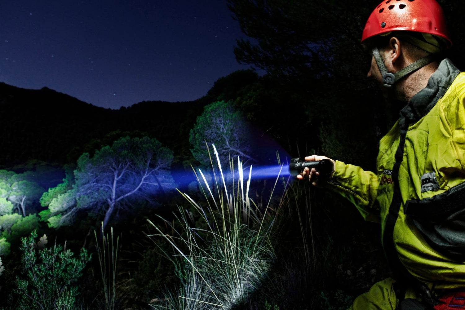 Person mit Stirnlampe und Fenix Taschenlampe beleuchtet Ufer und Bäume bei Nacht am See