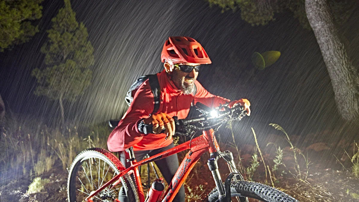Mann mit rotem Helm und Fahrrad in Regen bei Nacht mit heller Fenix Fahrradbeleuchtung im Wald