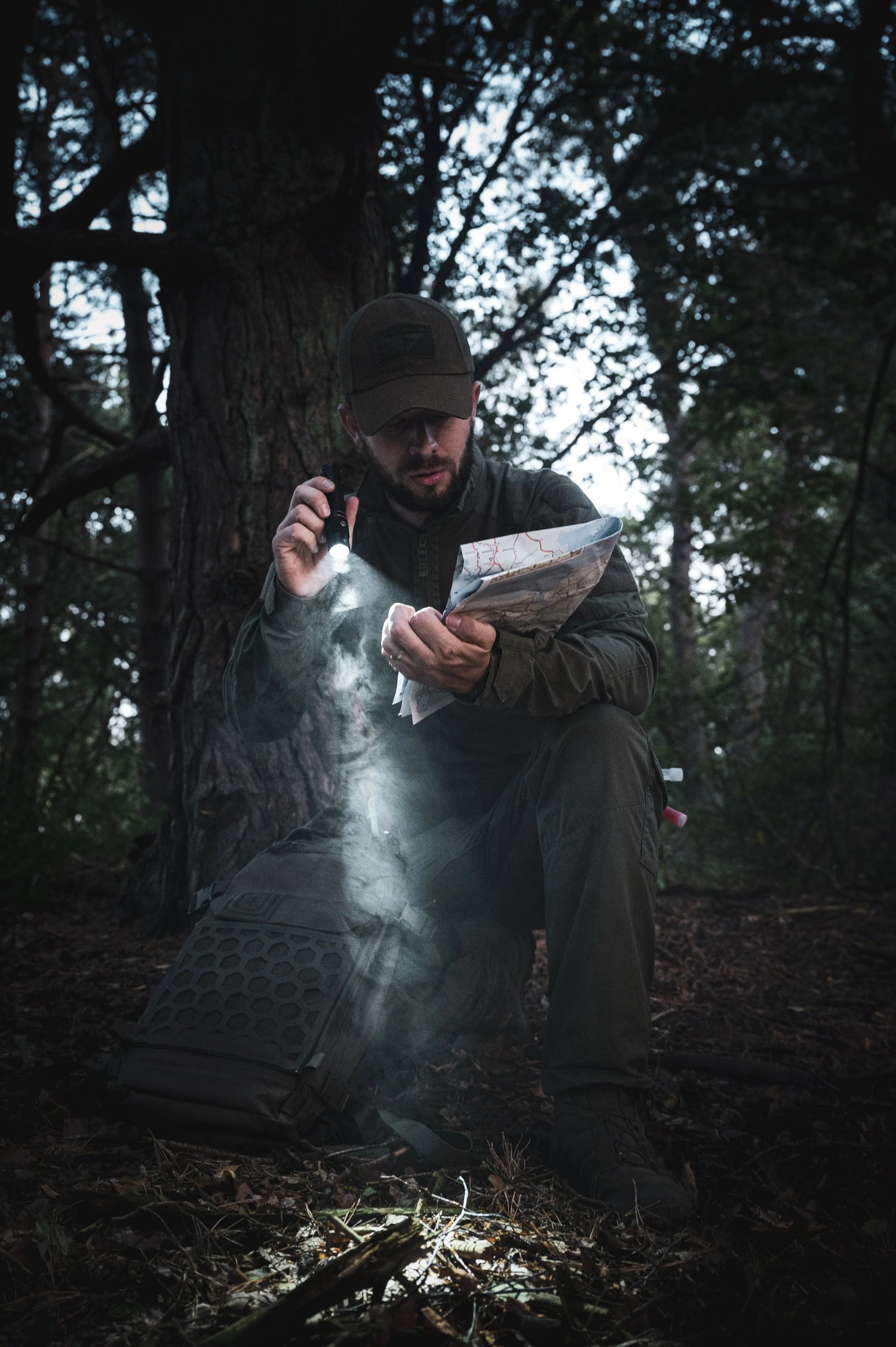 Mann mit Fenix-Taschenlampe liest Karte im dunklen Wald, Rucksack am Boden, Outdoor-Szene
