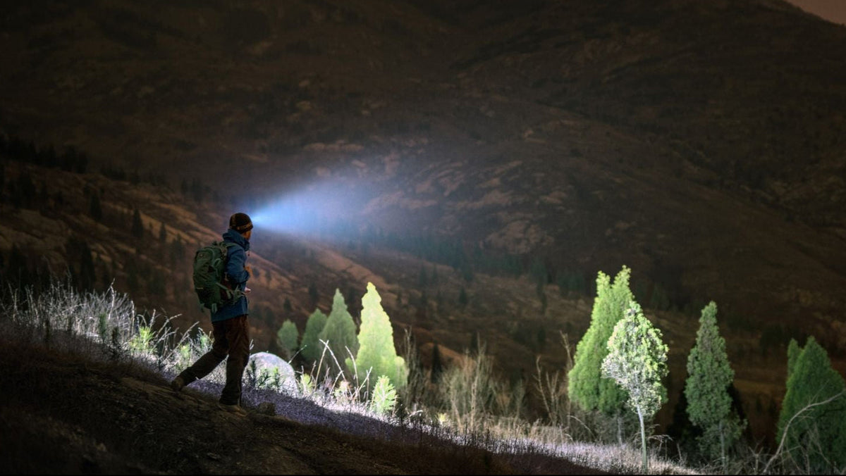 Stirnlampe im Outdoor-Einsatz bei Nacht: Wanderer nutzt leistungsstarke Fenix LED-Stirnlampe mit weitem blauen Lichtkegel beim herbstlichen Abstieg in den Bergen für maximale Sicherheit bei Dunkelheit.